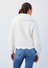 Load image into Gallery viewer, Person wearing a white quilted/swaeater jacket and blue jeans on a light gray background
