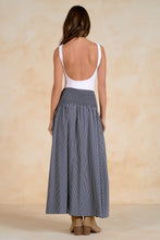 Load image into Gallery viewer, Woman wearing a white top and blue striped skirt against a beige background
