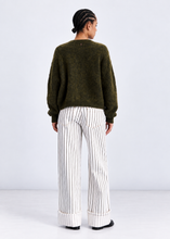 Load image into Gallery viewer, A model shown from the back wearing an olive green fuzzy knit sweater and white wide-leg trousers with thin black pinstripes, set against a plain light gray studio background.
