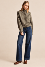 Load image into Gallery viewer, A woman modeling a cropped, high-neck, long-sleeve knit sweater in a heathered taupe-gray color, paired with dark blue wide-leg jeans and brown leather ankle boots, against a solid beige studio background.
