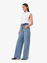 Load image into Gallery viewer, A woman modeling a pair of high-waisted, wide-leg light blue denim jeans with a white sleeveless top, shown from a side profile against a plain white studio background.
